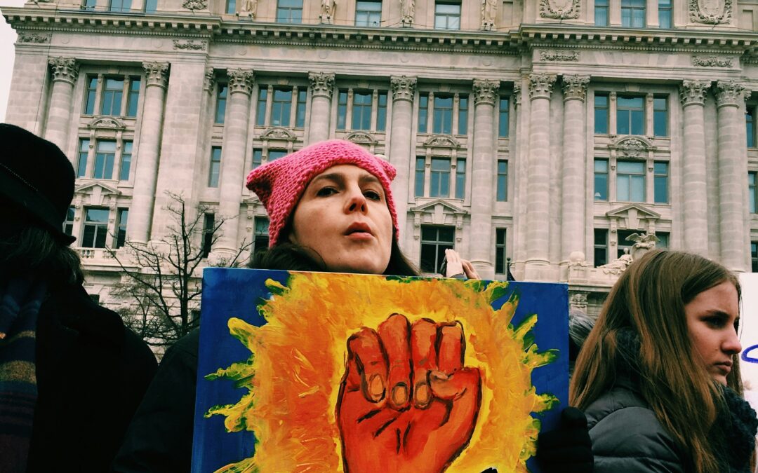 Ragazza che manifesta in pubblico, con un cartello raffigurante un pugno.
